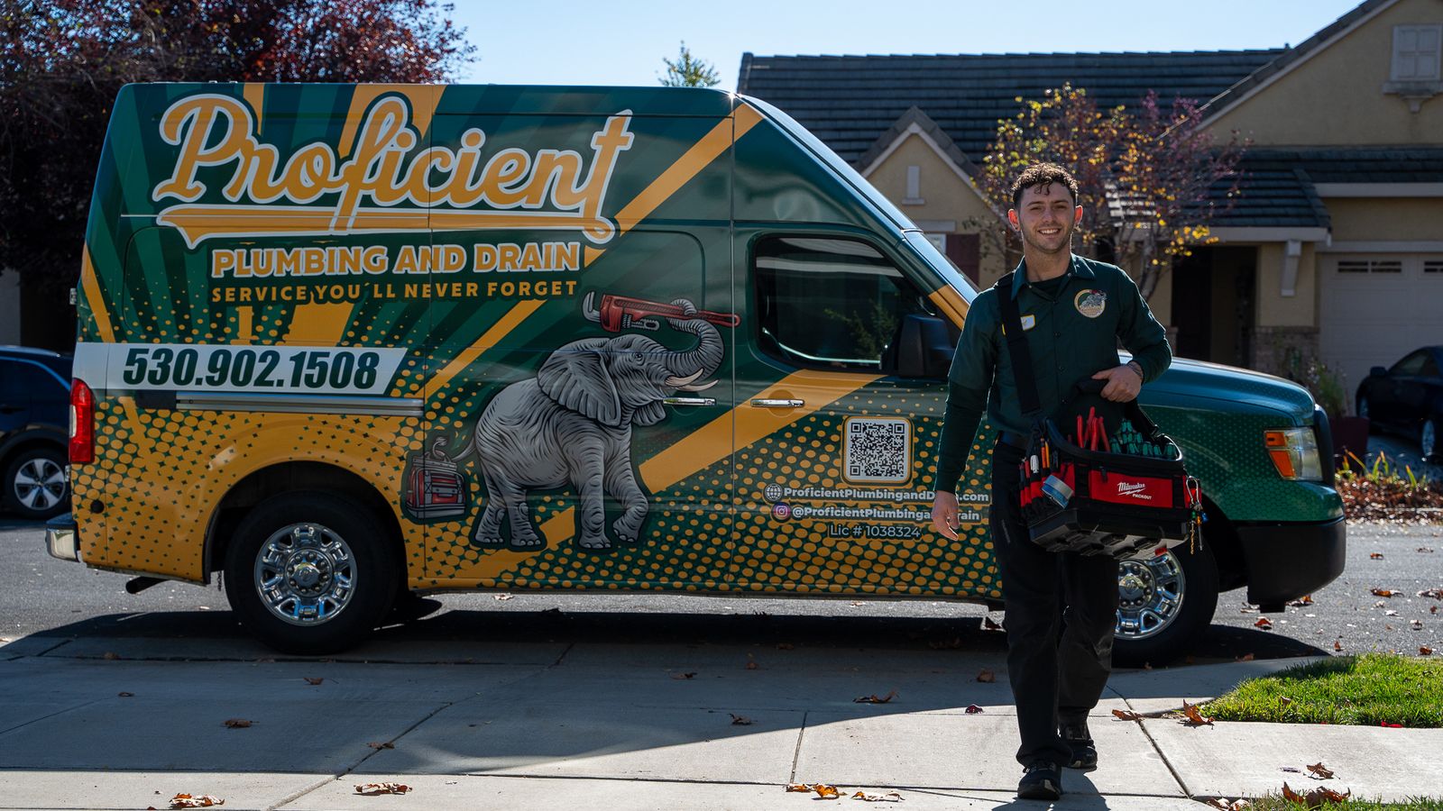 Proficient Plumbing and Drain technician beside a wrapped company van, with the elephant and pipe wrench livery clearly visible