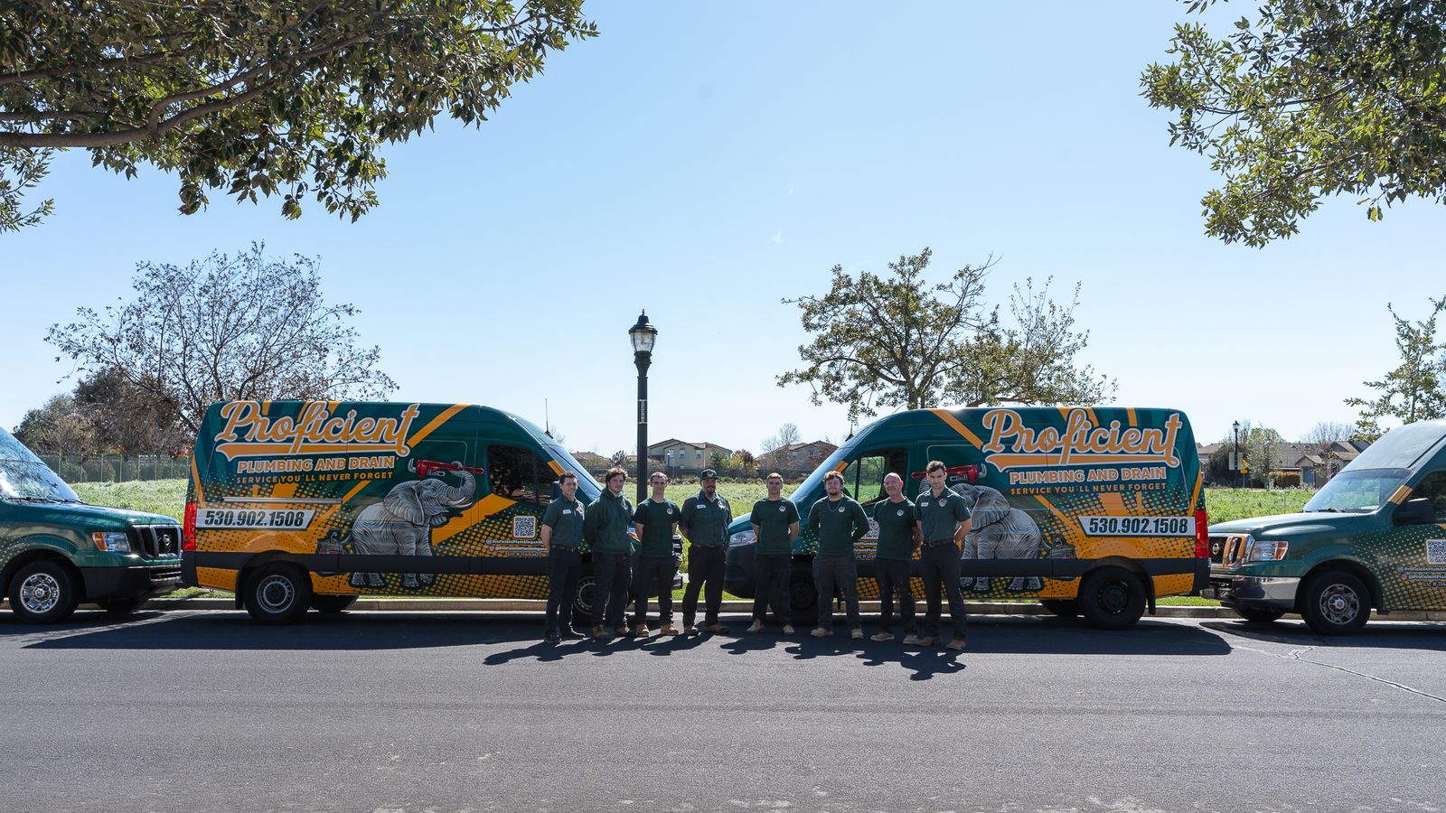 The Proficient Plumbing and Drain fleet of wrapped vans parked with the crew, under an open sky