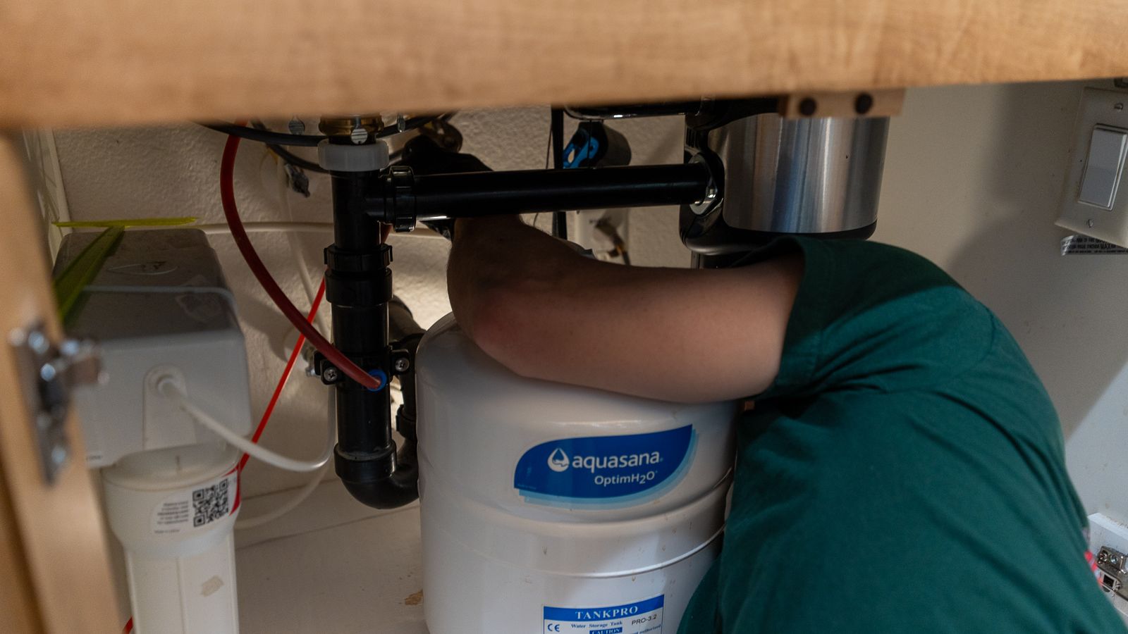 Under-sink view of a kitchen cabinet showing a water filtration canister plumbed in beside the disposal and P-trap