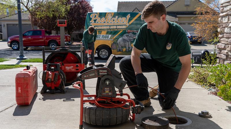 Proficient Plumbing technician running a drum machine at an open sewer cleanout on a Sacramento driveway