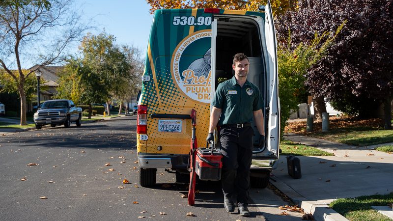 Proficient Plumbing technician lifting a tool case out of the open rear doors of a company van on a Sacramento street