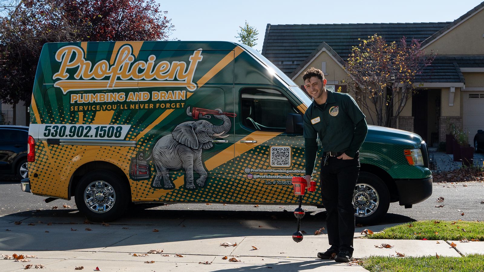 Proficient Plumbing technician looking up from an electronic line locator on a driveway, with the wrapped company van behind him