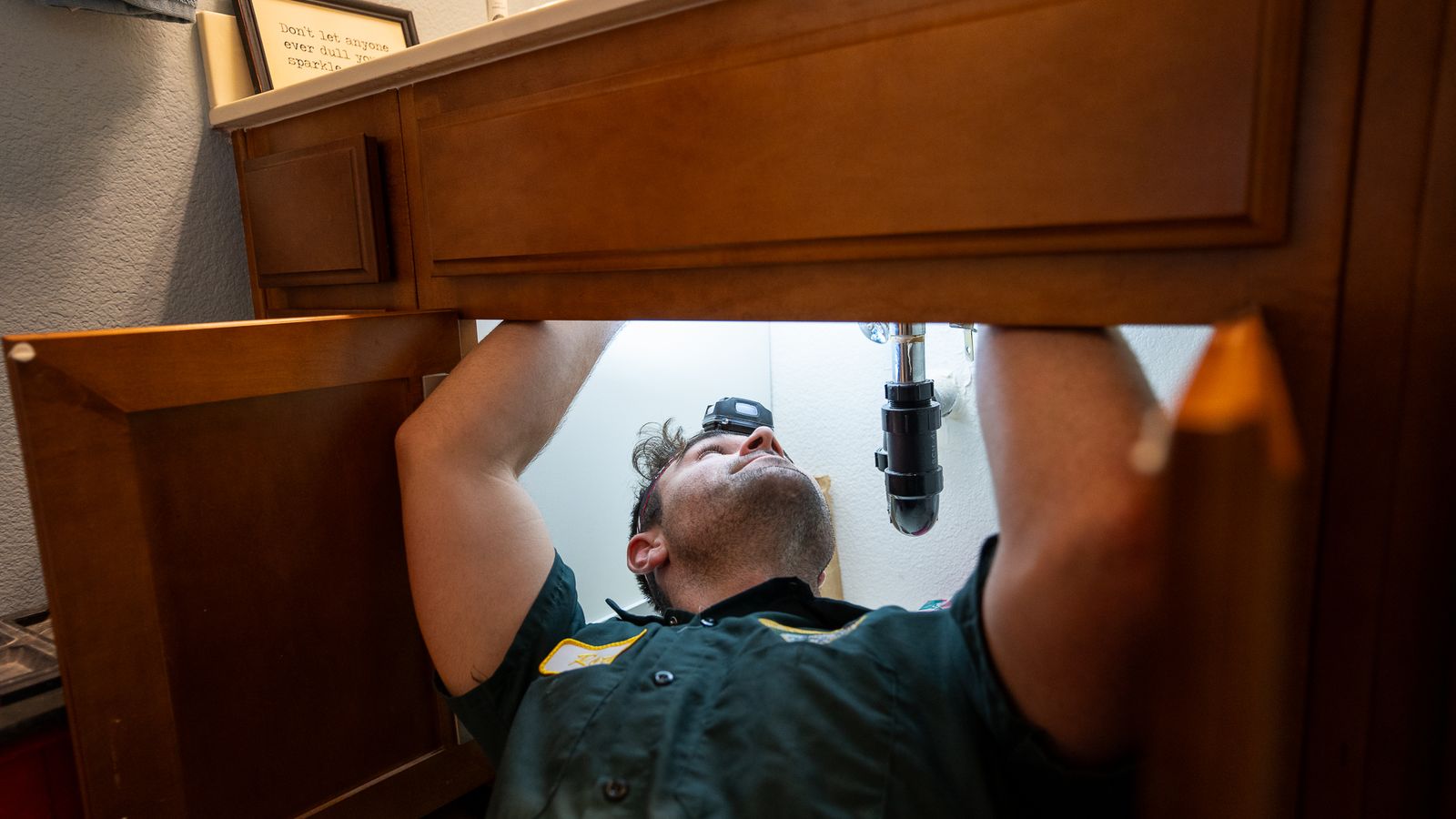 Proficient Plumbing technician lying on his back under a bathroom vanity working on the P-trap by headlamp