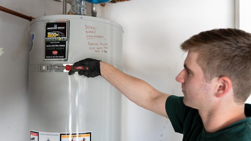 Plumber draining a residential tank water heater during a maintenance flush