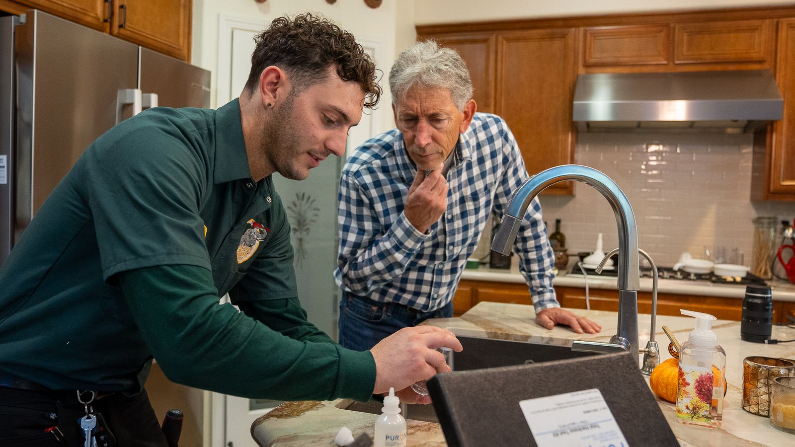 Proficient Plumbing technician running a water hardness test at a kitchen sink while the homeowner watches